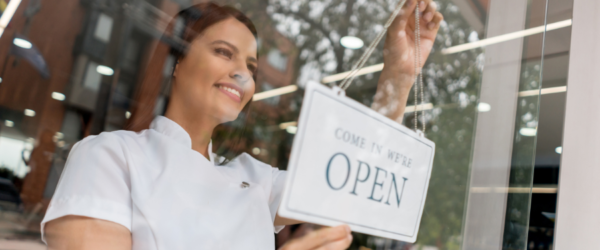 salon and spa business growth - a spa employee hanging an open sign in a window